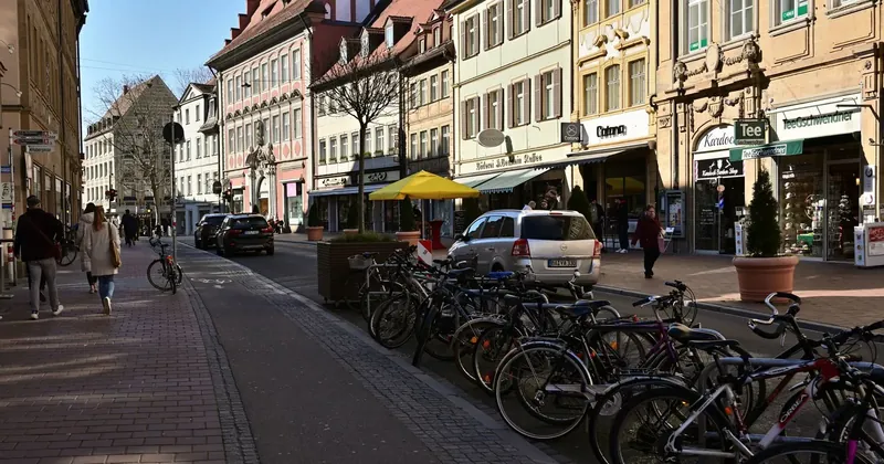 Městská ulice s chodci, obchody a zaparkovanými koly