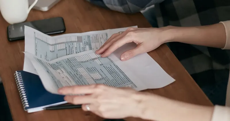 Ruce procházejí daňové formuláře na stole