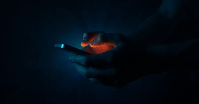 Ruce držící rozsvícený mobilní telefon ve tmě