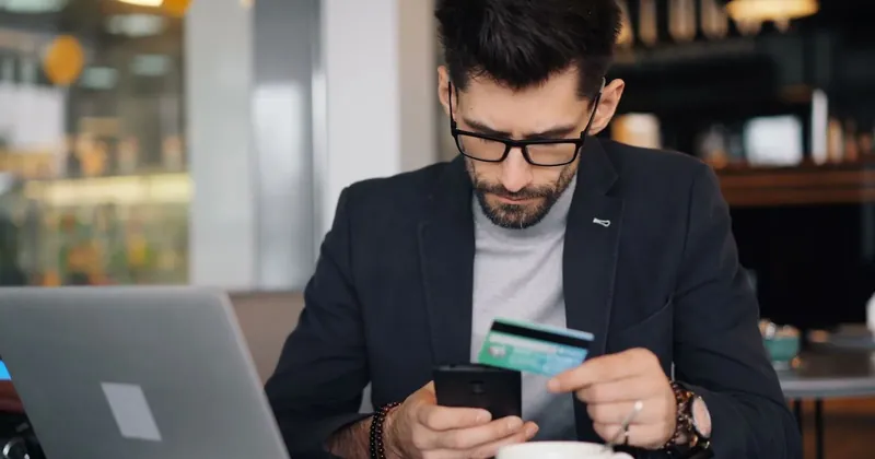 Muž kontroluje bankovní aplikaci v telefonu s kartou v ruce