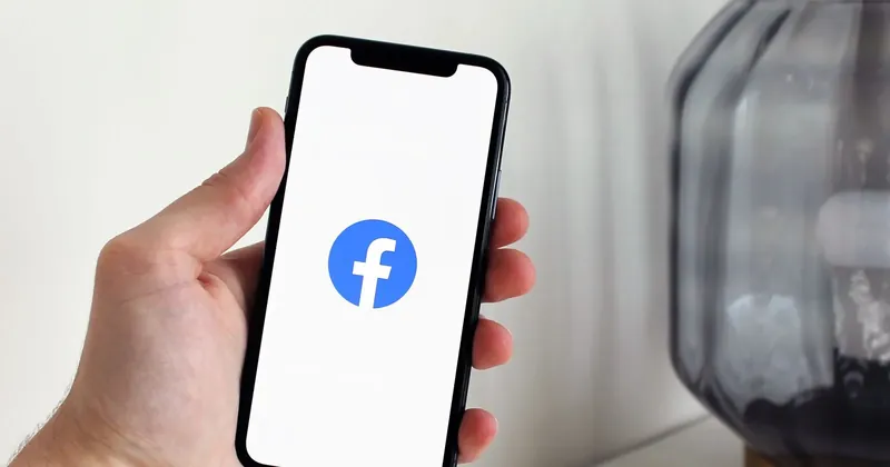 Ruka drží telefon s logem Facebooku