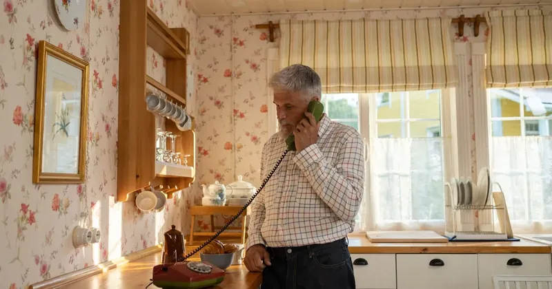 Starší muž telefonuje z pevné linky v kuchyni