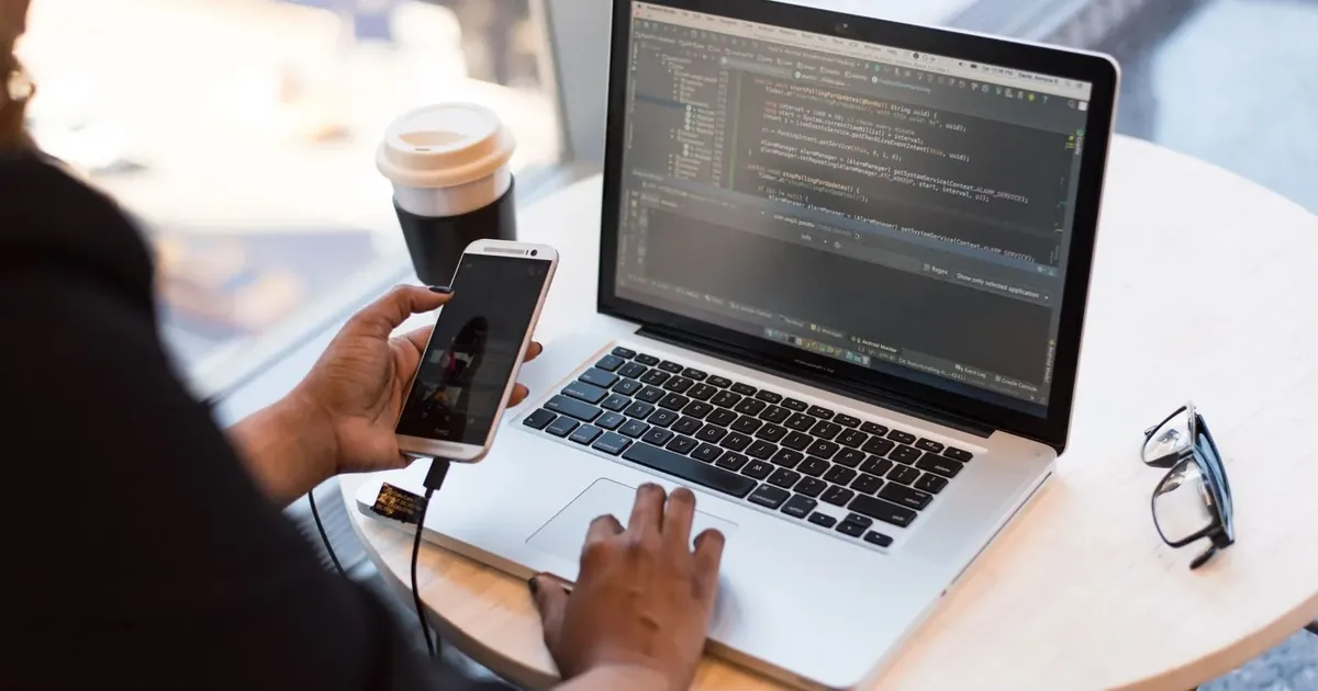 Muž drží telefon u notebooku s otevřeným programem