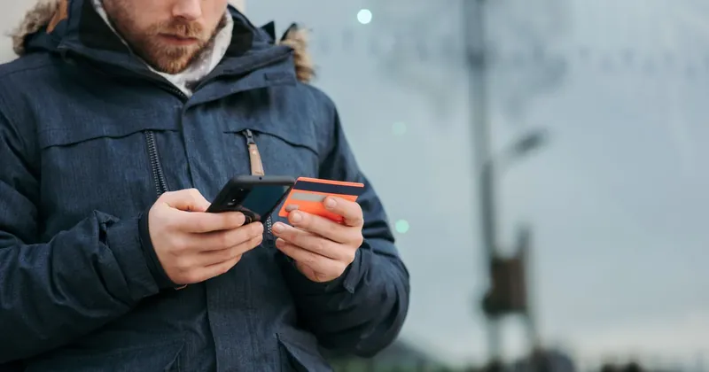 Muž venku kontroluje mobilní telefon s platební kartou v ruce