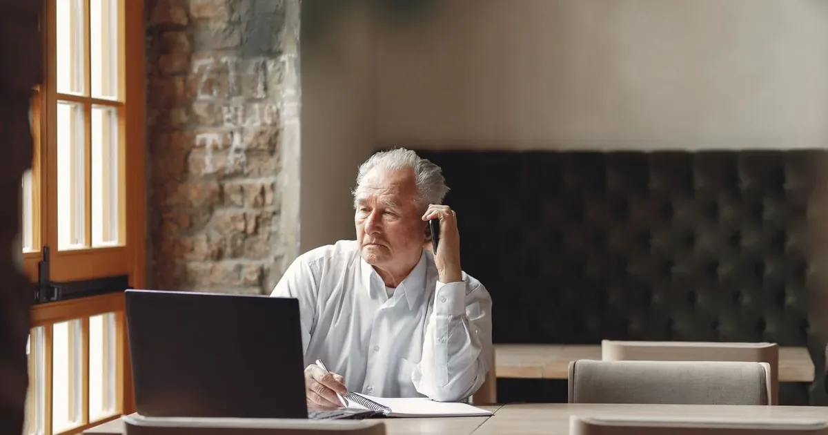 Starší muž telefonuje u notebooku