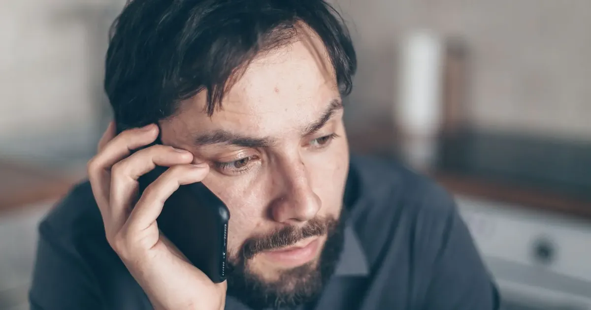 Muž s nejistým výrazem drží telefon u ucha