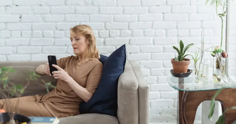 Žena středního věku čte zprávu v telefonu na pohovce
